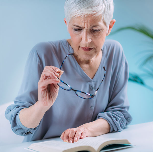 Frau hält Brille über Buch.